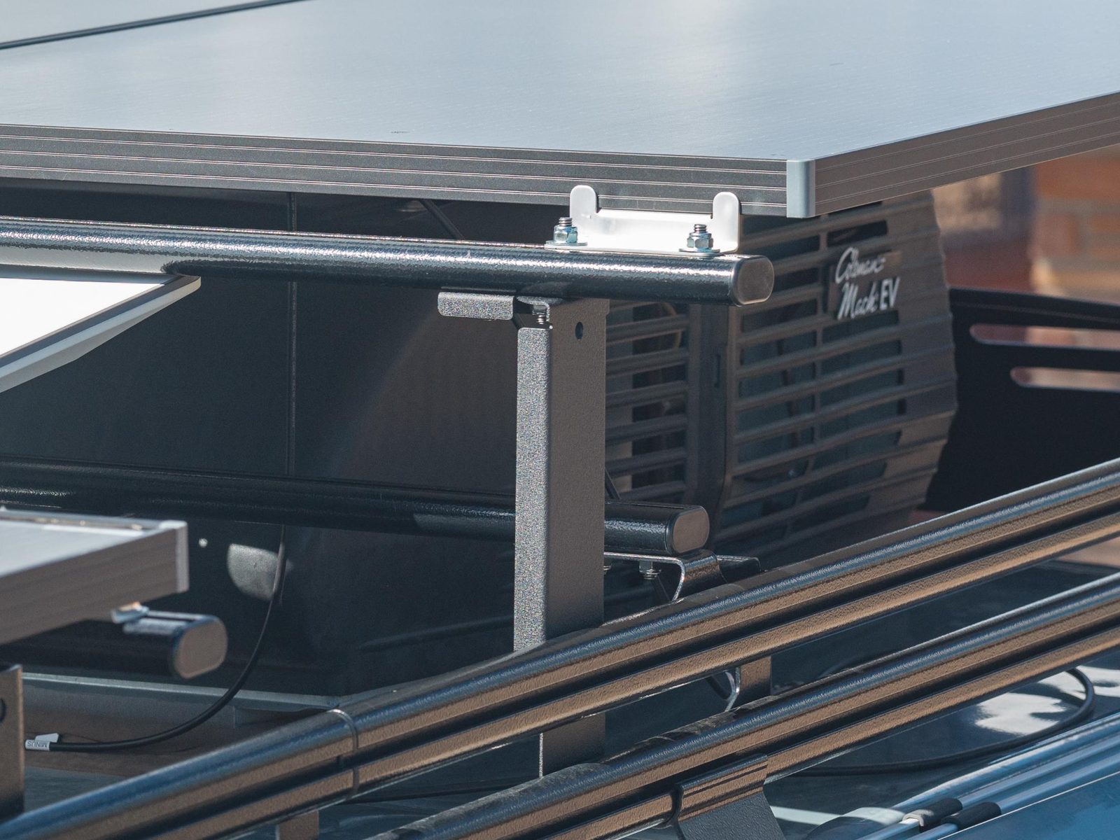 Close-up of a Mesa Riser bolted to the roof rack rails, holding a crossbar and solar panel above the A/C unit